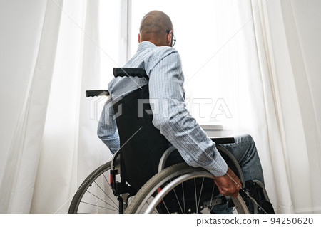 African american man in wheelchair sitting near the window alone at home 94250620