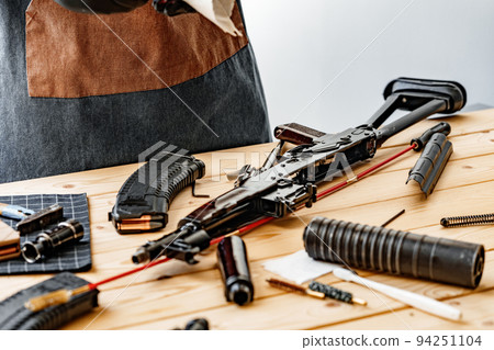 Close up of young man in apron disassembling a gun above the table 94251104