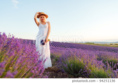 Young woman in long white dress standing in lavender field Young woman in long white dress standing in lavender field 94251136