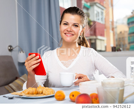 Young woman using phone at table with tea and peaches 94252612