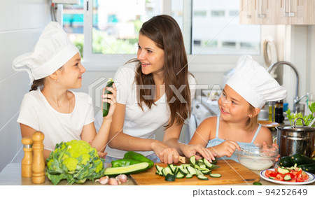 Portrait of little sisters with mother in caps learning how to cook 94252649