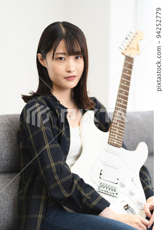 Woman sitting on sofa and playing guitar Woman sitting on sofa and playing guitar 94252779