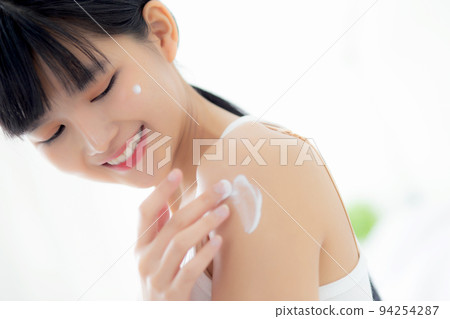 Beautiful young asian woman happy applying cream or lotion with moisturizer to skin on shoulder. 94254287