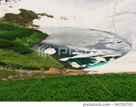 Mt. Norikura in summer Fusegaike Pond surrounded by pine trees and remaining snow 94256785