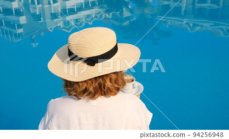 woman holds a white cup of coffee in her hands on the background of a blue swimming pool. Good 94256948
