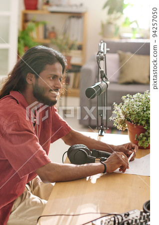 Young smiling man with dark long hair communicating with guest in studio Young smiling man with dark long hair communicating with guest in studio 94257050