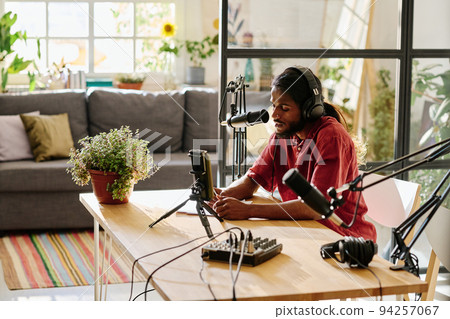 Young man in headphones sitting by desk and reading points of discussion Young man in headphones sitting by desk and reading points of discussion 94257067