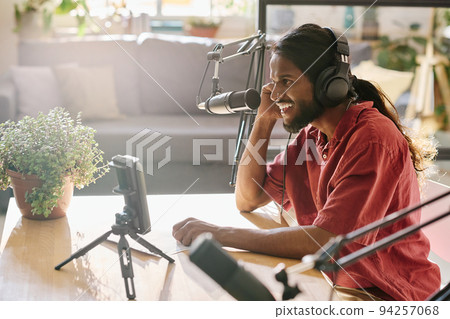 Side view of cheerful guy in casualwear and headphones talking in microphone Side view of cheerful guy in casualwear and headphones talking in microphone 94257068