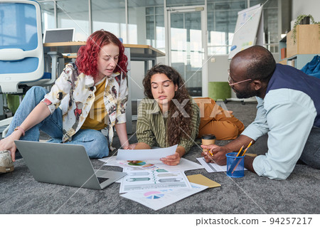 Young African American man listening to female colleagues discussing papers Young African American man listening to female colleagues discussing papers 94257217