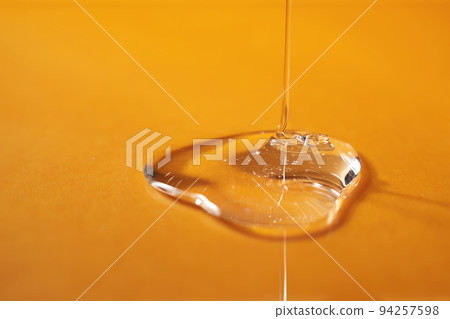 A drop of body gel or shampoo pouring from above on a yellow saturated background. 94257598