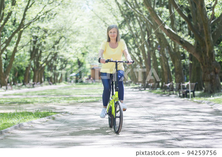 Active lifestyle. Senior beautiful sporty woman rides a yellow bicycle in the park, outdoors. He goes, looks at the camera, smiles 94259756