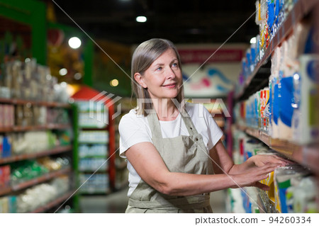 Senior female supermarket worker lays out the goods on the shelves 94260334