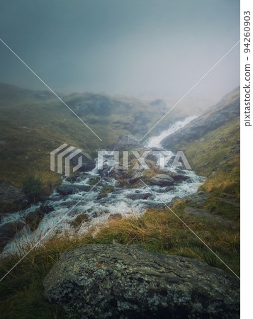 Mountain stream flowing fast across a rocky valley in Fagaras Mountains. River with high water debit during the rainy season Mountain stream flowing fast across a rocky valley in Fagaras Mountains. River with high water debit during the rainy season 94260903