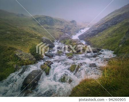Fast stream flowing across a rocky valley in Fagaras Mountains. River with waterfalls and dense mist landscape 94260905