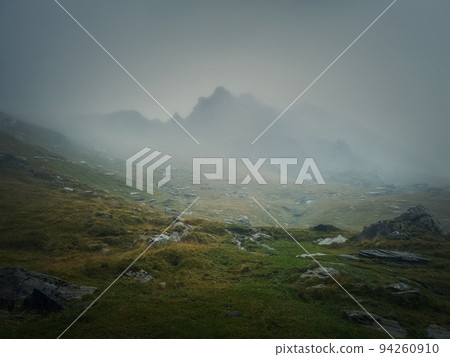 Mountain peak seen through the dense fog. Rainy scene in the mounts, hiking in the mist landscape Mountain peak seen through the dense fog. Rainy scene in the mounts, hiking in the mist landscape 94260910