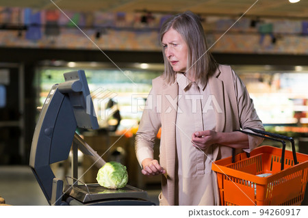 frustrated and sad senior woman weighs vegetables in supermarket frustrated and sad senior woman weighs vegetables in supermarket 94260917