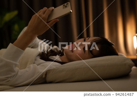 一個女人在床上/臥室裡操作智能手機 一個女人在床上/臥室裡操作智能手機 94261487