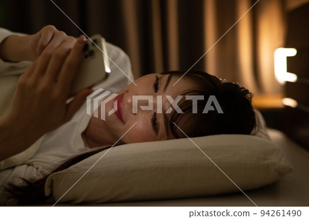 A woman operating a smartphone in bed / bedroom 94261490