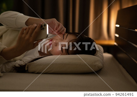 A woman who operates a smartphone while rubbing her eyes in a bed/bedroom A woman who operates a smartphone while rubbing her eyes in a bed/bedroom 94261491
