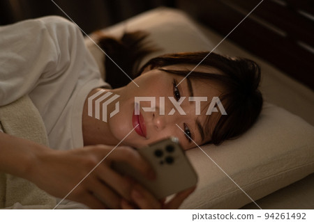 A woman operating a smartphone in bed / bedroom A woman operating a smartphone in bed / bedroom 94261492