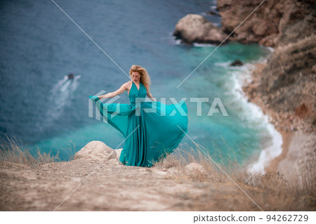 A woman in an emerald dress, a fashion model with long silk wings in a flowing dress, flying fabric on the embankment. A woman in an emerald dress, a fashion model with long silk wings in a flowing dress, flying fabric on the embankment. 94262729