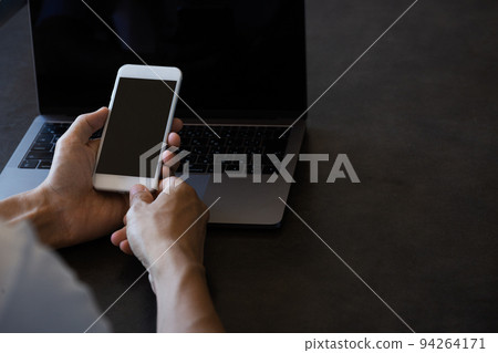 A man operating a smartphone in front of a laptop computer A man operating a smartphone in front of a laptop computer 94264171