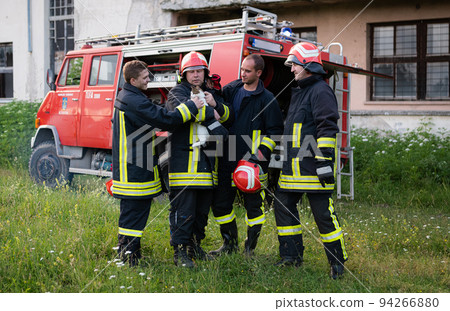 firefighters group in a protective suit and red helmet holds saved cat in his arms. Firefighter in fire fighting operation. firefighters group in a protective suit and red helmet holds saved cat in his arms. Firefighter in fire fighting operation. 94266880