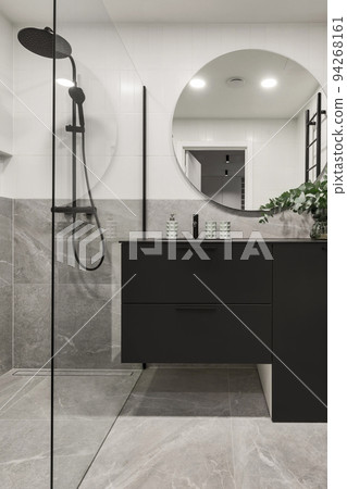 Modern minimalistic bathroom interior design with grey stone tiles, black furniture, eucalyptus in glass vase, round mirror. Aesthetic simple interior design concept. Modern minimalistic bathroom interior design with grey stone tiles, black furniture, eucalyptus in glass vase, round mirror. Aesthetic simple interior design concept. 94268161