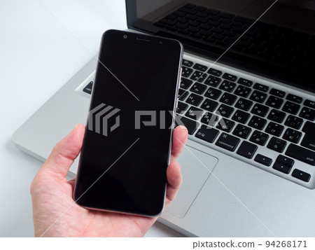 Hand holding a smartphone in front of a computer Hand holding a smartphone in front of a computer 94268171