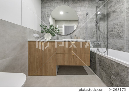 Modern minimalist bathroom interior design with wooden furniture, grey stone tiles, round mirror.  Aesthetic simple interior design concept. 94268173