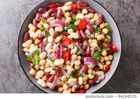 Three bean American picnic salad has cannellini beans, kidney beans, garbanzo beans, red onion, parsley and a sweet and sour dressing closeup in the plate. Horizontal top view 94268570