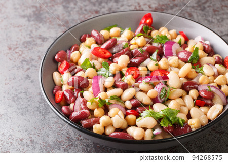 Three bean American picnic salad has cannellini beans, kidney beans, garbanzo beans, red onion, parsley and a sweet and sour dressing closeup in the plate. Horizontal Three bean American picnic salad has cannellini beans, kidney beans, garbanzo beans, red onion, parsley and a sweet and sour dressing closeup in the plate. Horizontal 94268575