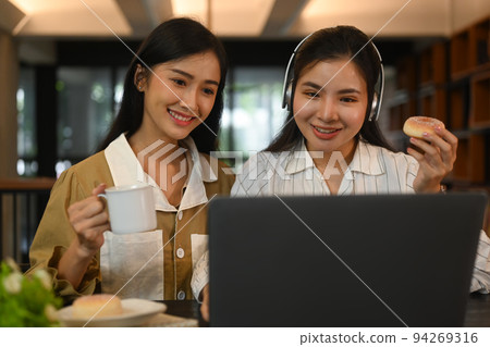 Two smiling women preparing for exams, learning together in modern college library. Education, people and technology concept Two smiling women preparing for exams, learning together in modern college library. Education, people and technology concept 94269316