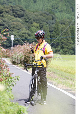 一個男人在騎自行車時停下來看著他的智能手機 一個男人在騎自行車時停下來看著他的智能手機 94269682