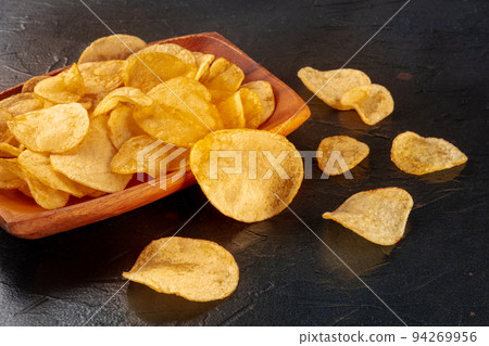 Potato chips or crisps in a bowl and scattered on a black stone background 94269956
