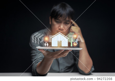 Tablet in hand of a man contemplating buying his first home with a preview of the house displayed above the tablet screen. first home buying idea. selective focus on tablet.  94272208