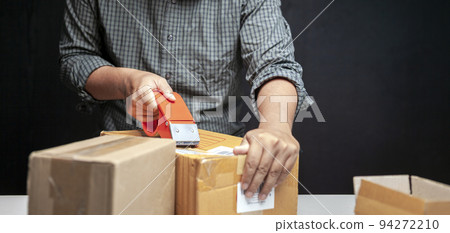 A man is packing a small box of his online business in his room at home. A man is packing a small box of his online business in his room at home. 94272210