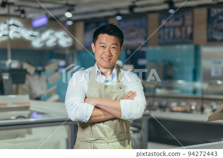 portrait of handsome asian man salesman in apron standing and looking at camera in grocery store supermarket. Male worker seller or small business owner. indoor. food, groceries market Cheerful smile 94272443