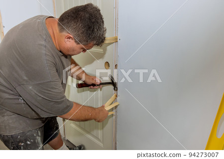 As part of the process of installing interior doors in a new house, a trim worker uses a hammer to strike the door jambs 94273007