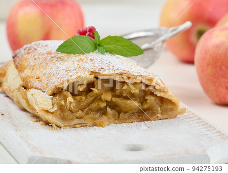 Baked strudel with apples sprinkled with powdered sugar on a white wooden board, delicious dessert Baked strudel with apples sprinkled with powdered sugar on a white wooden board, delicious dessert 94275193