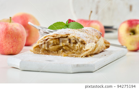 Baked strudel with apples sprinkled with powdered sugar on a white wooden board Baked strudel with apples sprinkled with powdered sugar on a white wooden board 94275194