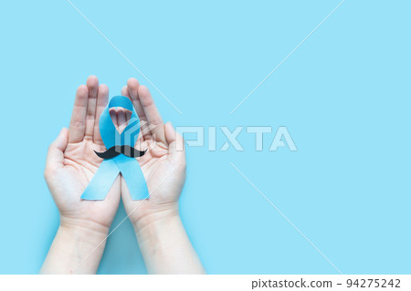 Men's health and Prostate cancer awareness campaign in November. Man hands holding light blue ribbon awareness with mustache on blue background. Symbol for support men who living with cancer. Men's health and Prostate cancer awareness campaign in November. Man hands holding light blue ribbon awareness with mustache on blue background. Symbol for support men who living with cancer. 94275242