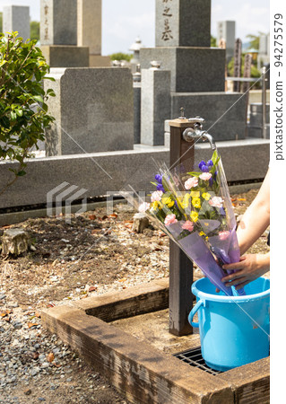A senior woman who came to visit and clean the grave is pouring water into the bucket 94275579