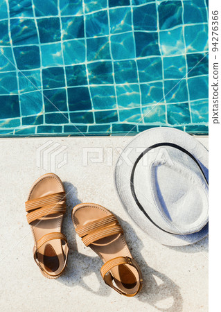 Vacation flat lay with woman's sandals and hat front of the pool Vacation flat lay with woman's sandals and hat front of the pool 94276366