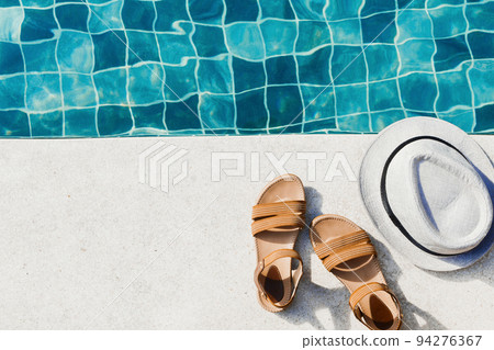 Vacation flat lay with woman's sandals and hat front of the pool Vacation flat lay with woman's sandals and hat front of the pool 94276367