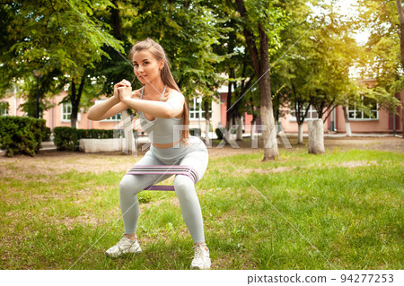 A beautiful young woman is engaged in a sports field in the park. Fitness, workout, outdoor. Solar glare, stretch gum, sports equipment. Trained muscular body and butt. Girl smiles, happy A beautiful young woman is engaged in a sports field in the park. Fitness, workout, outdoor. Solar glare, stretch gum, sports equipment. Trained muscular body and butt. Girl smiles, happy 94277253