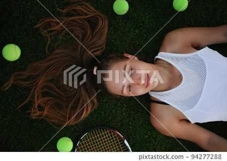 Portrait of a beautiful young woman. Sports tennis court, outdoor recreation. Fitness body, weight loss, active lifestyle, rest after training. Sunset, summer. racket balls on the grass Portrait of a beautiful young woman. Sports tennis court, outdoor recreation. Fitness body, weight loss, active lifestyle, rest after training. Sunset, summer. racket balls on the grass 94277288