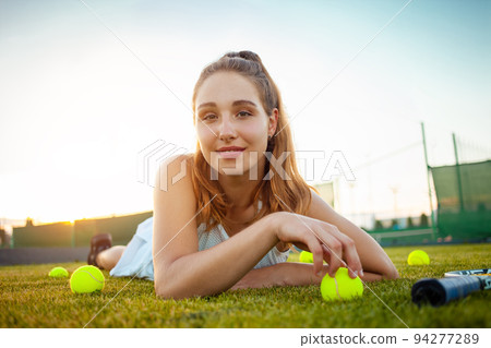 Portrait of a beautiful young woman at sunset. Tennis court, athletic body. Fitness, weight loss, athlete smiles, happy. Active lifestyle in the open air. Sunny glare, enjoyment balls on the grass Portrait of a beautiful young woman at sunset. Tennis court, athletic body. Fitness, weight loss, athlete smiles, happy. Active lifestyle in the open air. Sunny glare, enjoyment balls on the grass 94277289