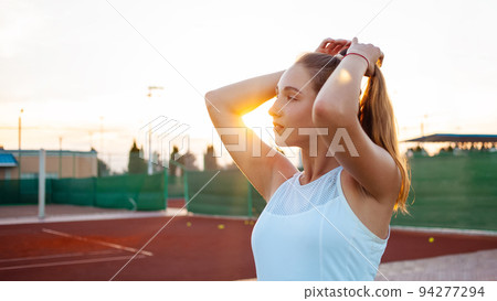 Portrait of a beautiful young woman at sunset. Tennis court, athletic body. Fitness, weight loss, athlete smiles, happy. Active lifestyle in the open air. Sunny glare, enjoyment outdoor Portrait of a beautiful young woman at sunset. Tennis court, athletic body. Fitness, weight loss, athlete smiles, happy. Active lifestyle in the open air. Sunny glare, enjoyment outdoor 94277294