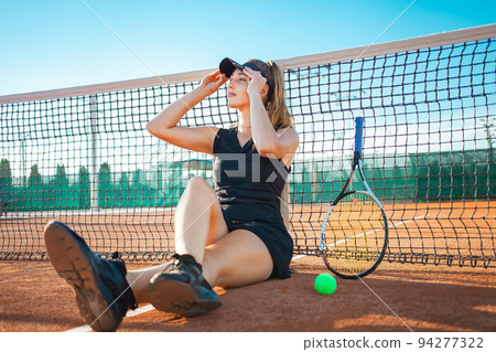Portrait of a woman on the court. Tennis stadium, athlete with racket and ball. Sports grid. The girl rests after training. Active lifestyle, outdoor. Sunny day, summer. sunset. Smiles, happiness Portrait of a woman on the court. Tennis stadium, athlete with racket and ball. Sports grid. The girl rests after training. Active lifestyle, outdoor. Sunny day, summer. sunset. Smiles, happiness 94277322
